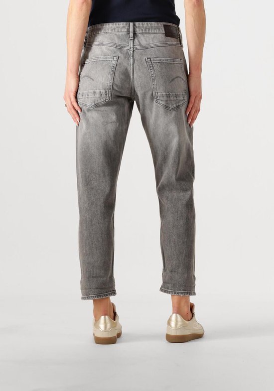 Achterkant van vrouw in grijze G-Star jeans met opgerolde broekspijpen en gouden sneakers.