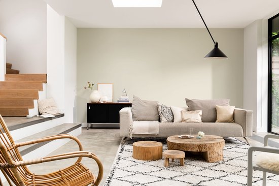 Een lichte woonkamer met een beige bank, houten salontafel en rotan stoel.