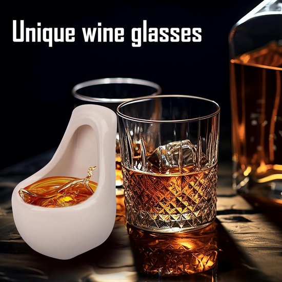 Uniek urinoir-vormig borrelglaasje gevuld met amberkleurige drank, naast een whiskyglas met ijs.