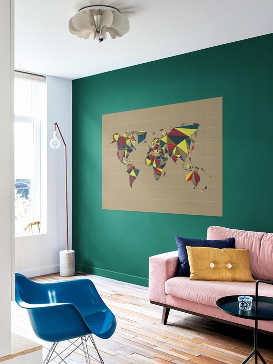 Carte du monde abstraite en polygones multicolores sur fond taupe, accrochée à un mur vert au-dessus d'un canapé rose.