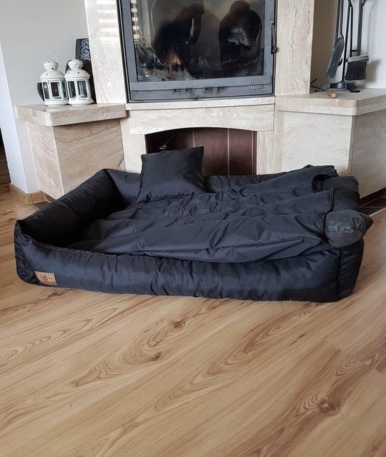 Coussin pour chien noir sur un plancher en bois, devant une cheminée, avec un coussin et une couverture.