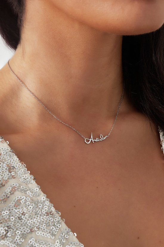 Une femme porte un collier argenté avec le mot 'Amsterdam' en écriture élégante.
