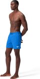 Homme debout de profil, portant un short de bain Speedo bleu.