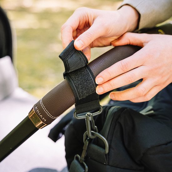 Mains attachant un clip noir pour poussette au guidon d'une poussette.