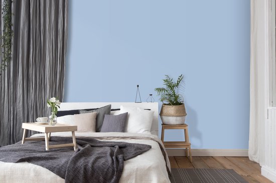 Lichtblauwe muurverf in een slaapkamer met een gestyled bed en grijze gordijnen.