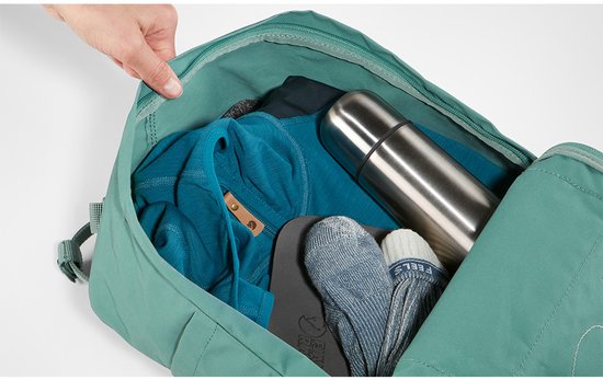Donkergroene rugzak geopend met kleding, thermosfles en sokken erin.