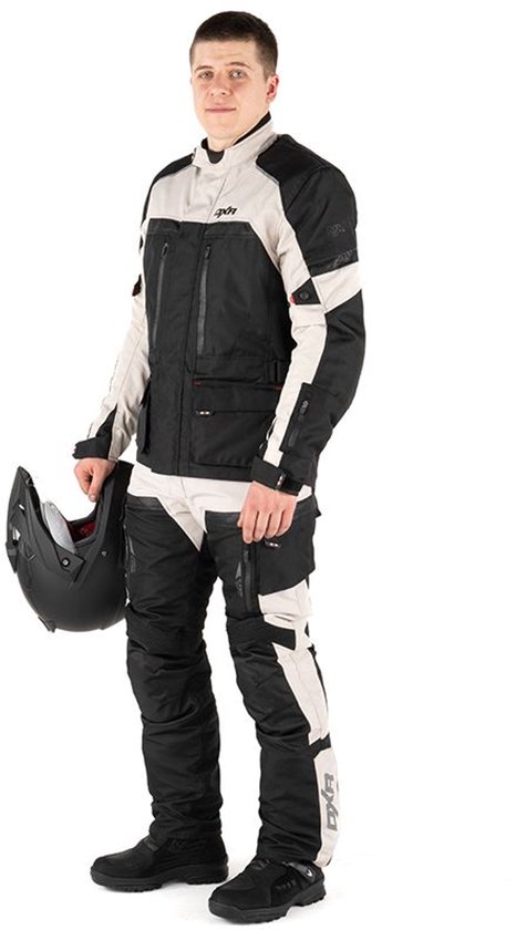 Man in DXR motorpak, zwart/grijs jack en broek, met helm en handschoenen. Staand.