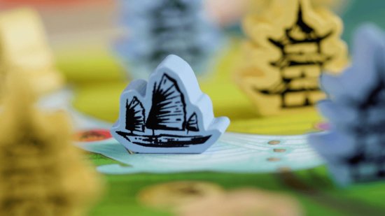 Blauw houten speelfiguur in de vorm van een Chinese jonk op een bordspel met groene heuvels.