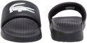 Twee zwarte slider slippers, één met krokodillenprint, één met 'LACOSTE' op de zool.