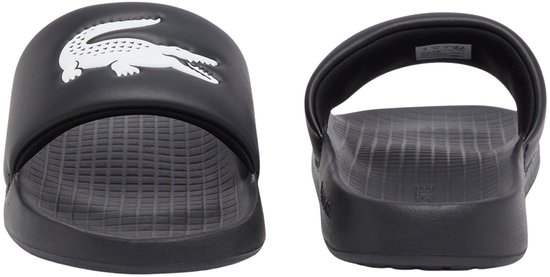 Twee zwarte slider slippers, één met krokodillenprint, één met 'LACOSTE' op de zool.