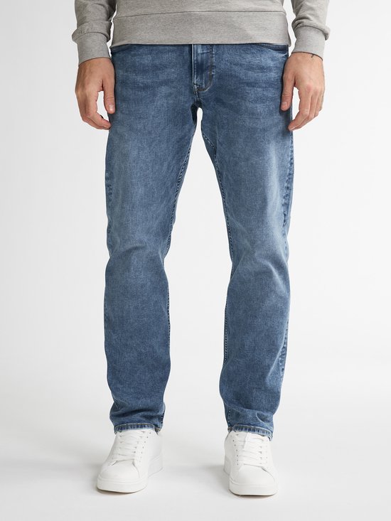 Man in een lichtblauwe jeans en witte sneakers. De jeans heeft een normale pasvorm.