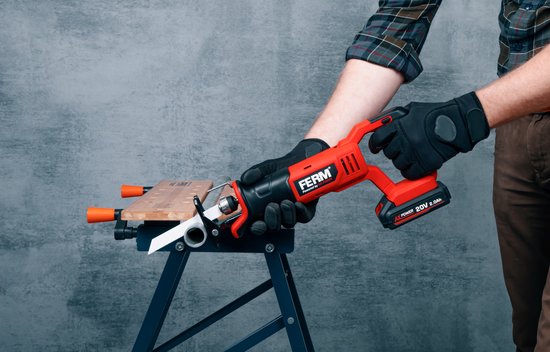 Man met handschoenen zaagt met een rode en zwarte reciprozaag een plank en een grijze buis.