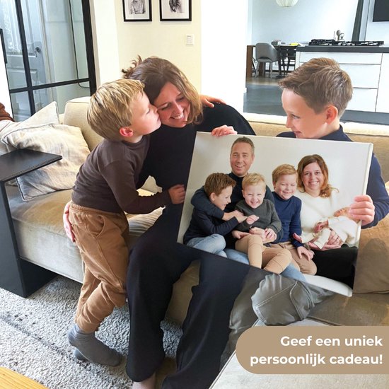 Een gezin houdt een canvas schilderij met hun foto's vast op een bank, met de tekst 'Geef een uniek persoonlijk cadeau!'
