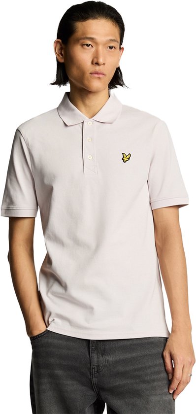 Man met lichtroze poloshirt met geel vogel-logo en grijze jeans.