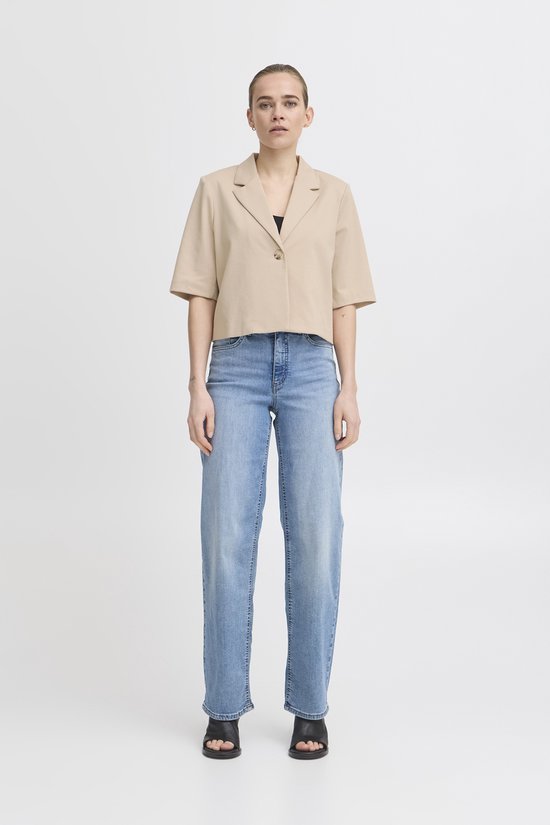 Model draagt een beige cropped blazer met korte mouwen en één knoopsluiting, met een spijkerbroek.