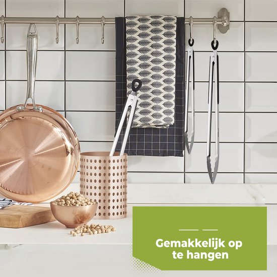 RVS tang met zwarte greep hangt aan een haakje in een keuken, naast koperen pan en kikkererwten.