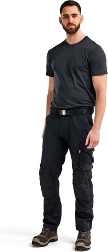 Homme portant un t-shirt gris foncé et un pantalon de travail noir avec poches, debout.