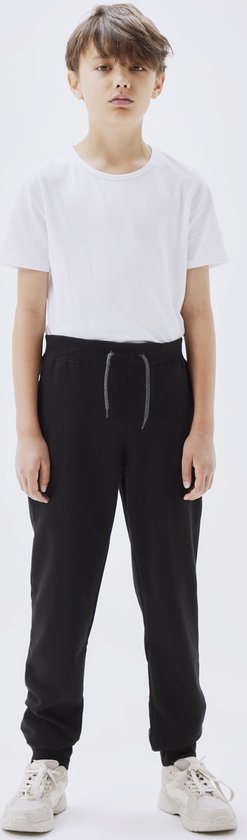 Jongen in wit t-shirt en zwarte joggingbroek met grijze veter, staand