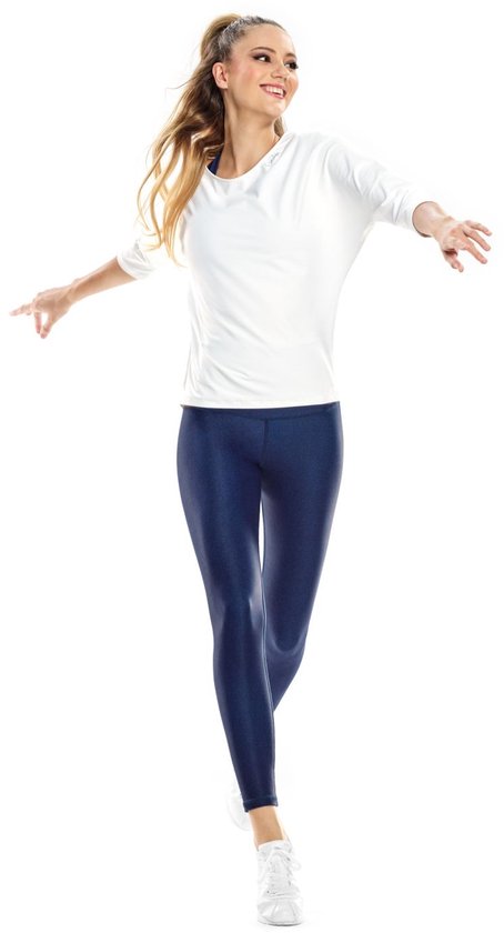 Vrouw in witte driekwart top en donkerblauwe glanzende legging, witte sneakers.
