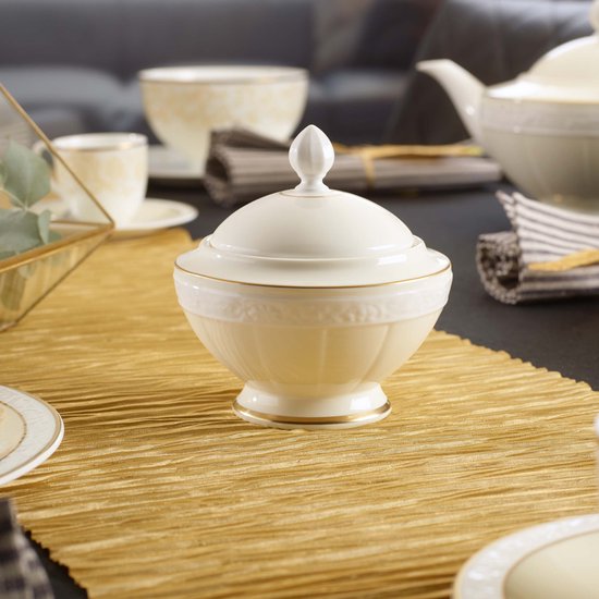 Sucrier crème avec couvercle blanc et accents dorés sur la table.