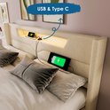 Gros plan de la tête de lit d'un lit beige avec éclairage LED intégré et ports de chargement USB & Type C, avec un téléphone en charge.