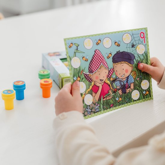 Een kind met een spelkaart waarop Fien & Teun worden getoond die bijen onderzoeken. Oranje, blauwe en groene stempels liggen op de tafel.