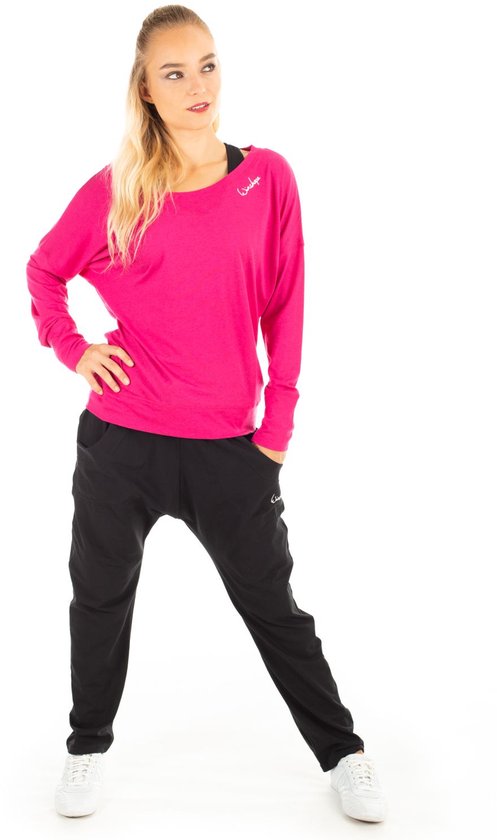 Model in een roze longsleeve met wijde boothals en een zwarte broek met logo.