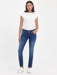 Model met een witte t-shirt draagt een donkerblauwe, nauwsluitende jeans en witte sneakers.
