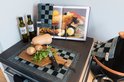 Keukendecor met tajine, groenten, flesjes olijfolie en kookboek, met grijs-zwart geblokte placemat.