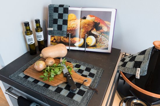 Keukendecor met tajine, groenten, flesjes olijfolie en kookboek, met grijs-zwart geblokte placemat.