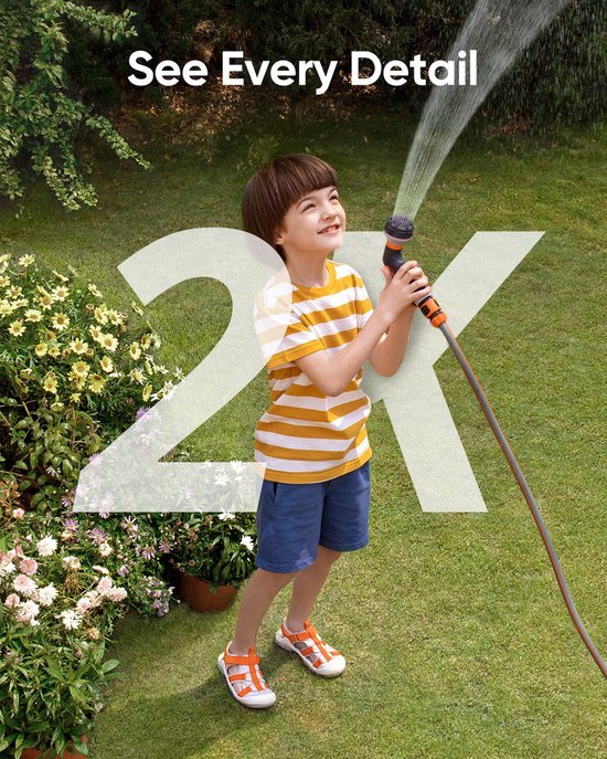 Jongetje met gestreepte t-shirt sproeit water in de tuin met een tuinslang.