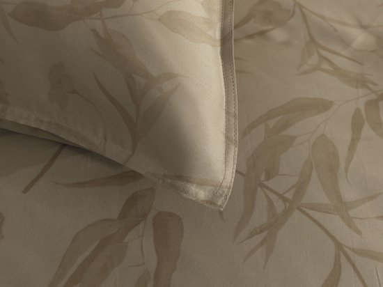 Close-up van een beige kussensloop met een subtiel bladermotief.