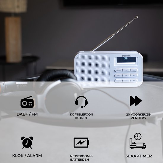 Witte Denver DAB+ radio met antenne, op een tafel geplaatst met koptelefoon en lach. Iconen tonen DAB+/FM, koptelefoonuitgang, 20 voorkeuzezenders, klok/alarm, netstroom & batterijen en slaaptimer.