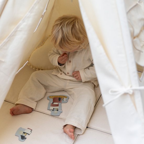Detailopname van een jong kind zittend in een crèmekleurige tipi tent, kijkend naar speelgoed op de grond.