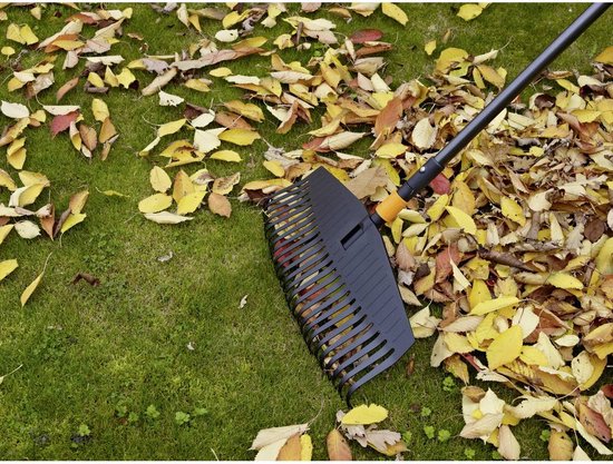 Zwarte Fiskars bladhark met oranje accent, veegt herfstbladeren op groen gras.