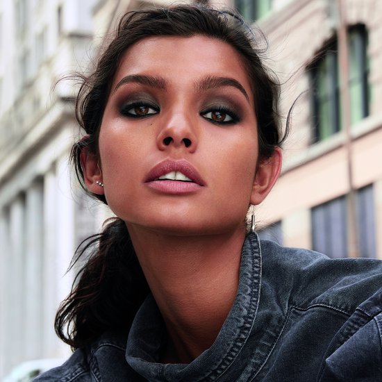 Model met smokey eye make-up en een denim jasje, op de achtergrond een stedelijke omgeving.