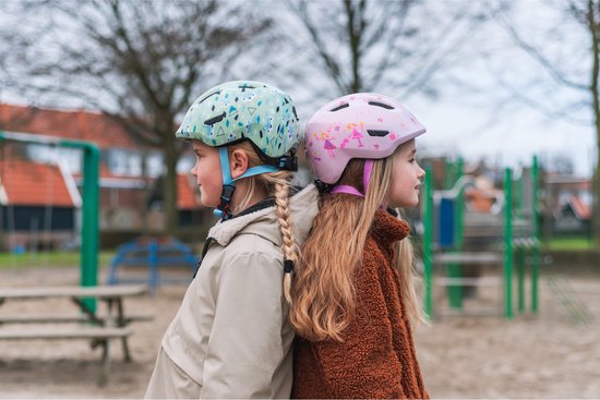 Twee helmen op een grijze bank. Een lichtgroene met winter/dierenmotief en een roze met bloemenmotief.