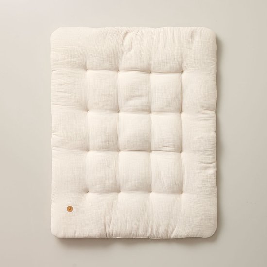 Crème, rechthoekig, capitonne speelkleed met kleine houten knoop rechtsonder.
