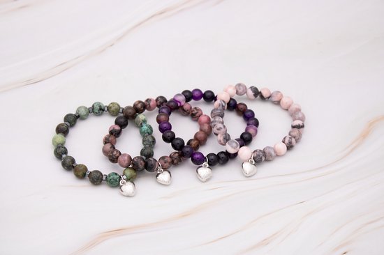 Vier armbanden met gekleurde kralen en zilverkleurige hartjes, liggend op een witte achtergrond.