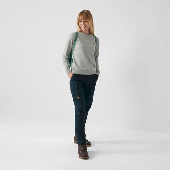 Vrouw met een grijze sweater en donkerblauwe broek draagt een turquoise Kånken rugzak.