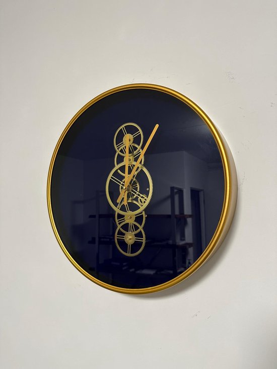 Ronde wandklok met een mat gouden rand en donkerblauwe wijzerplaat. De klok heeft gouden tandwielen die draaien en gouden wijzers.