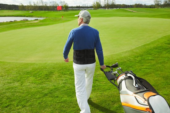Man met grijze pet en blauwe trui met Bracefox rugbrace op golfbaan.