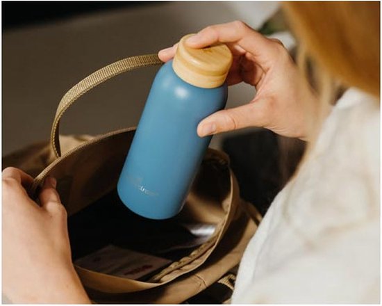 Blauwe fles met houten dop wordt in tas gestopt.