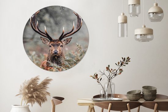 Een woonkamer met een muurcirkel van een hert met geweien, een bijzettafel met vazen en een stoel.