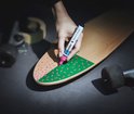 Hand met roze stift maakt stippen op groen vlak van skateboard.