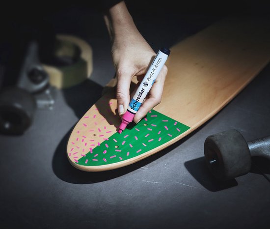 Hand met roze stift maakt stippen op groen vlak van skateboard.
