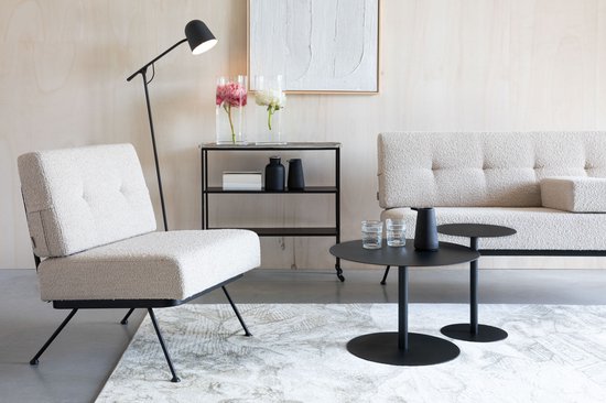 Zitje in beige bouclé stof met zwart metalen frame, naast een salontafel en een vloerlamp.