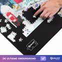 Close-up van een hand die een puzzelstukje plaatst op een zwarte puzzelmat met een gedeeltelijk gemaakte puzzel.