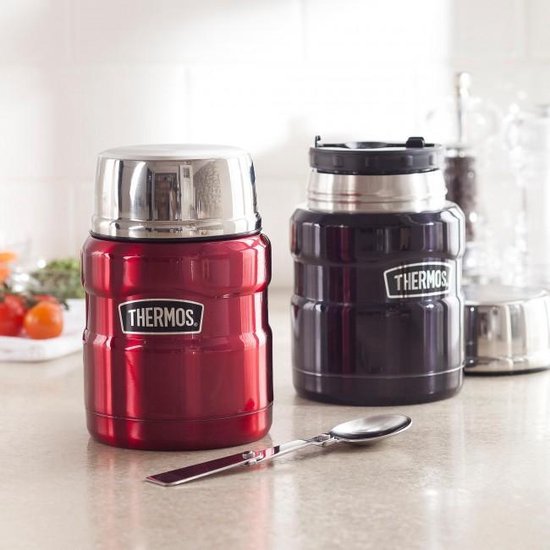 Deux contenants alimentaires Thermos, un rouge, un noir, avec des couvercles argentés et une cuillère au premier plan.