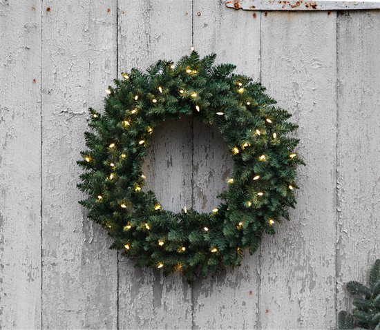 Donkergroene kerstkrans met warme witte lampjes, opgehangen aan een verweerde houten deur.